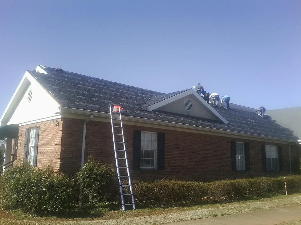 Crew tearing shingles off a brick ranch roof with a ladder set — Emergency Roof Repair work by our crew in Mount Pocono