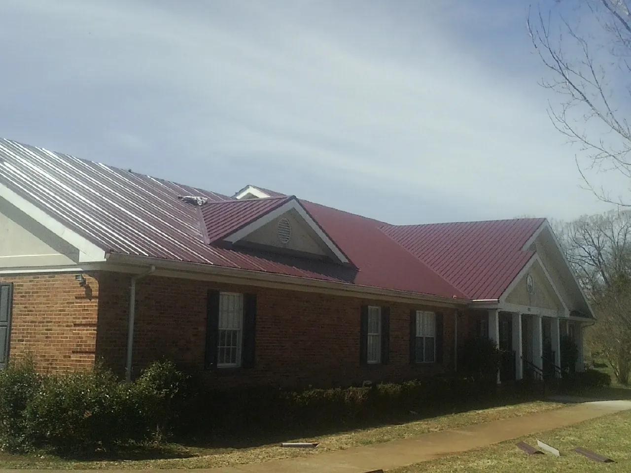 Red metal roof with gabled entries on a long brick building, from a Hail Damage Roof Repair job in Mount Pocono