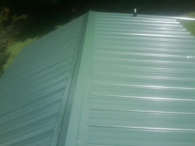 New green metal panels meeting at the ridge of a roof — Flat Roof Repair work by our crew in Mount Pocono