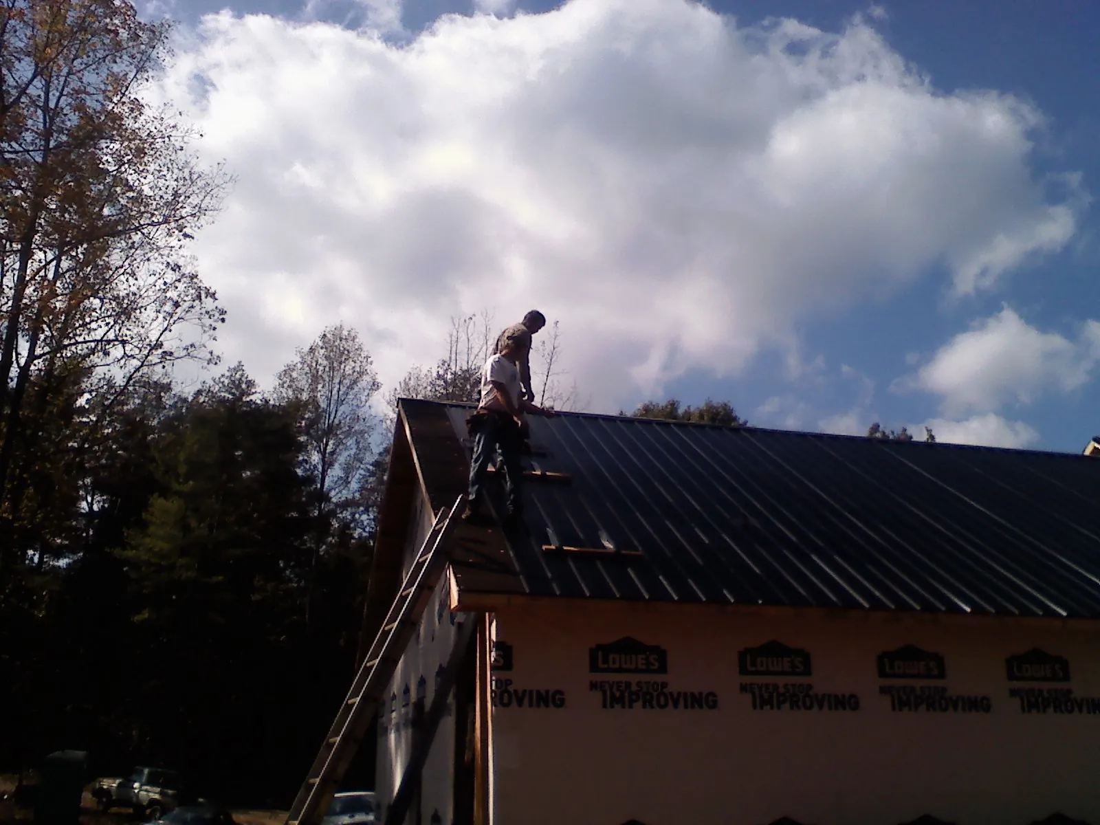 Roofer fastening dark metal panels high against a cloudy sky, from a Roof Inspection job in Mount Pocono