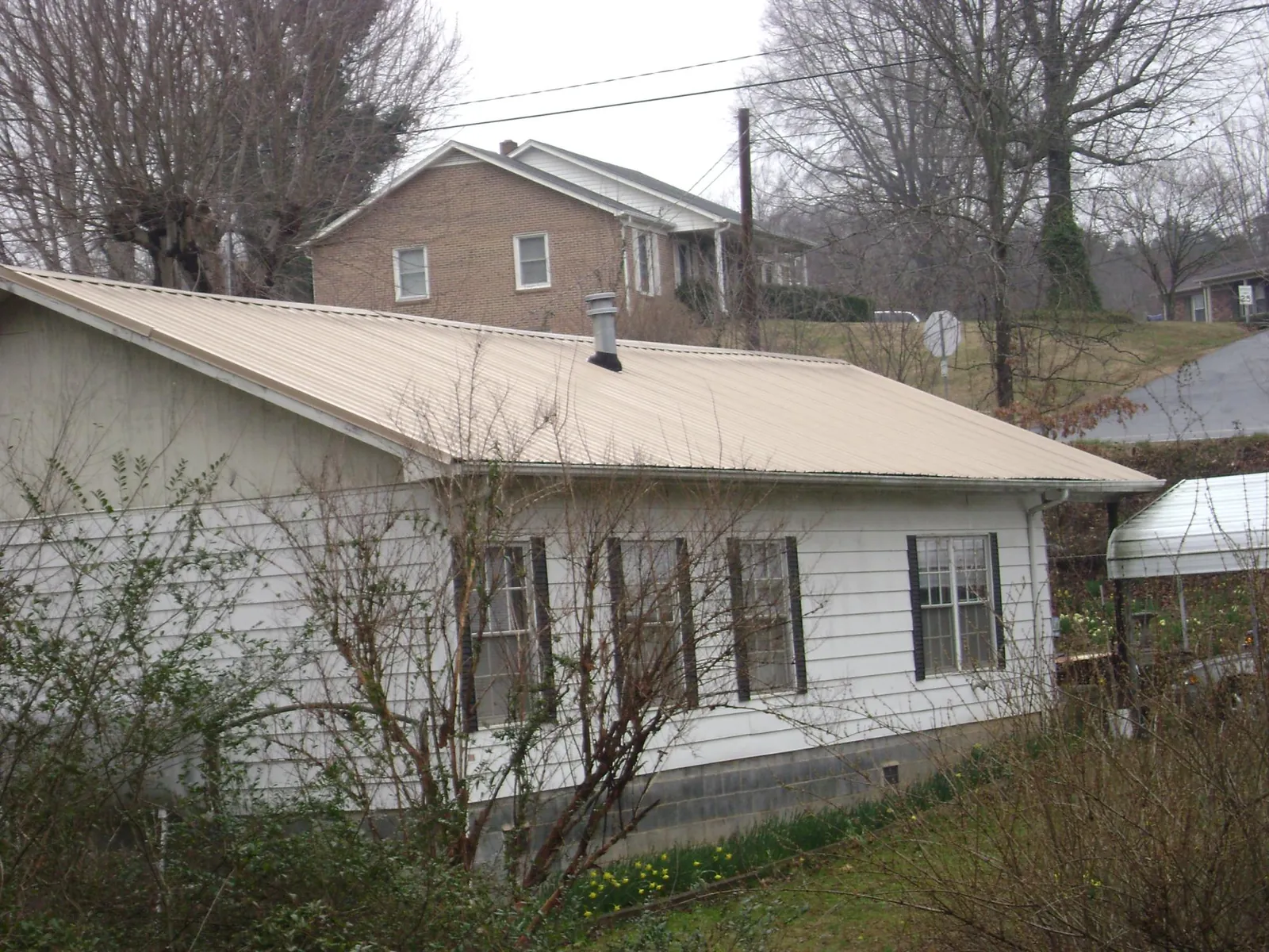 Tan metal roof on a white sided house set into a hillside — Commercial Roofing by Roofing Brothers in Mount Pocono